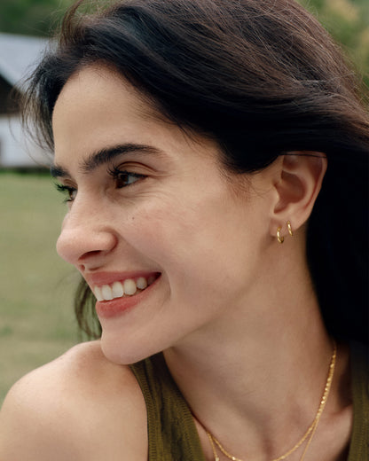 Gold mini huggie hoop earrings paired with layered earrings